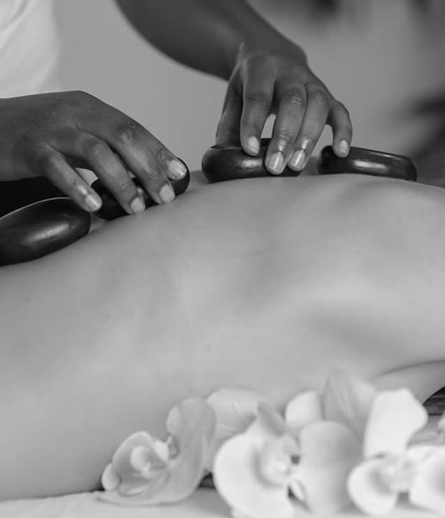 Professional hot stone massage therapy at a Lake District spa, skilled therapist placing heated basalt stones on client's back with white spa towels, showcasing traditional therapeutic massage treatments and holistic wellness services available at Lake District spa hotels and retreats