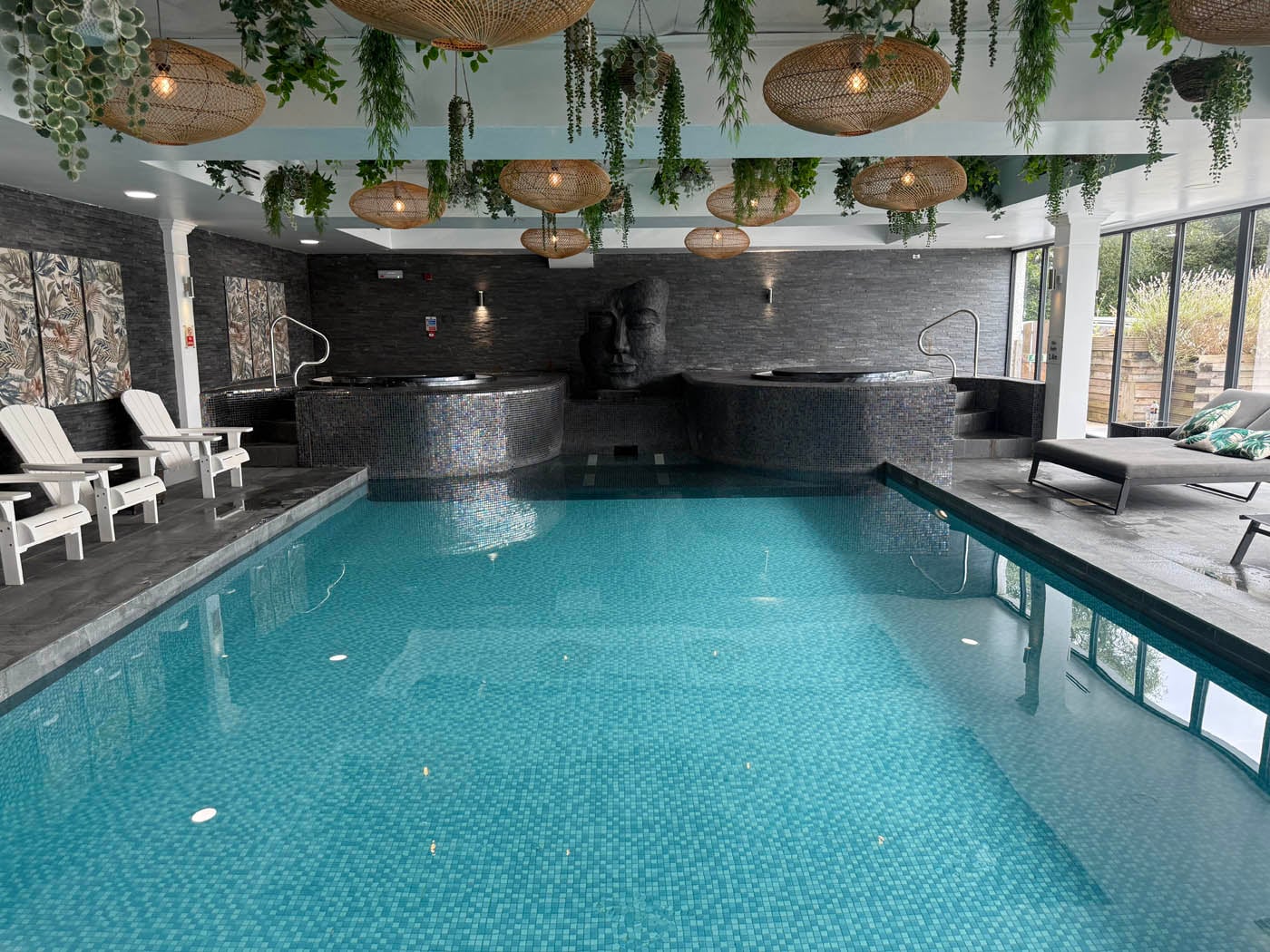 Botanical-inspired indoor pool at Beech Hill Hotel and Spa near Windermere, featuring natural woven pendant lights, cascading artificial greenery from ceiling, dark slate mosaic walls, turquoise heated pool, and contemporary nature-themed wellness design in the Lake District
