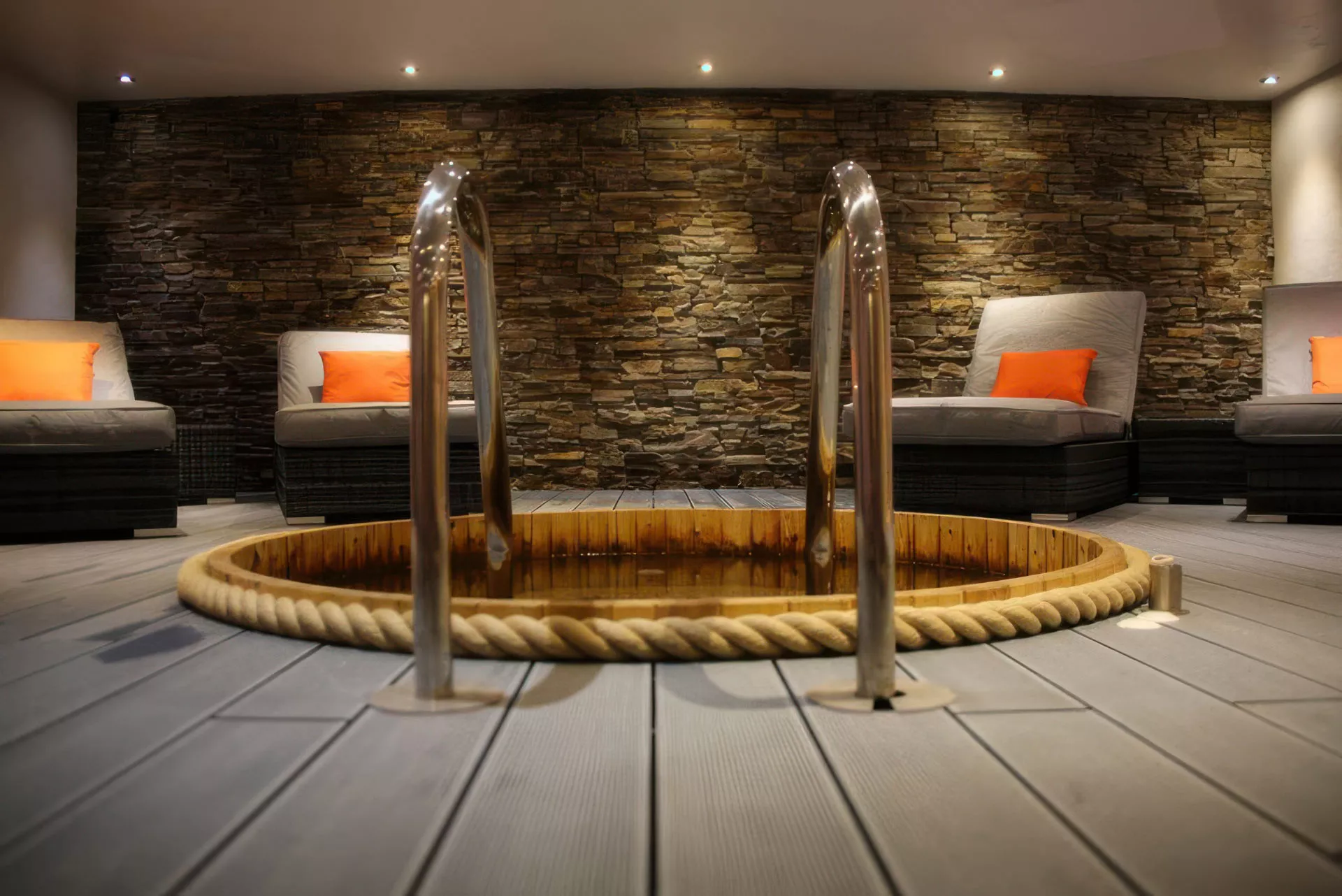 Unique circular Kneipp footbath at Netherwood Hotel and Spa in Grange-over-Sands, featuring natural rope-wrapped wooden basin design with dual cascade water features, positioned against authentic Lakeland dry stone walling with designer loungers and orange accent cushions