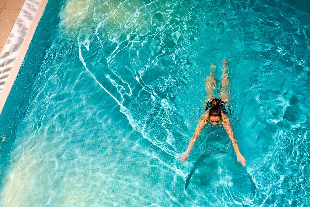 Aerial view of the turquoise swimming pool at Underscar luxury cottages near Keswick, showing crystal-clear heated waters with light ripple patterns and mosaic tiling, part of the relaxing spa and leisure facilities at this self-catering retreat beneath Skiddaw in the Lake District