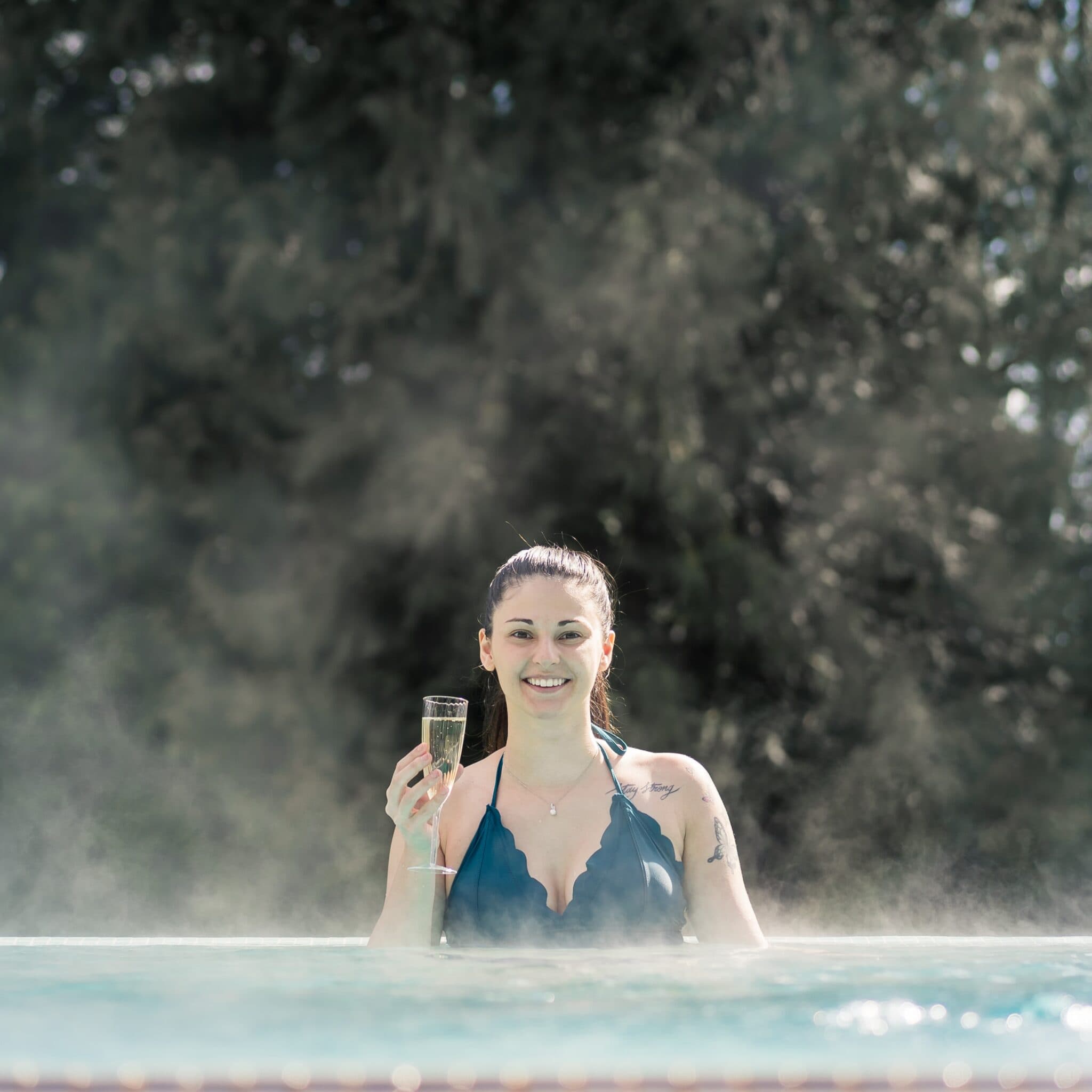 Guest celebrating with champagne in outdoor hydrotherapy pool at Armathwaite Hall Hotel and Spa, surrounded by thermal steam and ancient woodland near Bassenthwaite Lake, perfect for special occasions and romantic spa breaks in the Lake District Armathwaite Hall Spa
