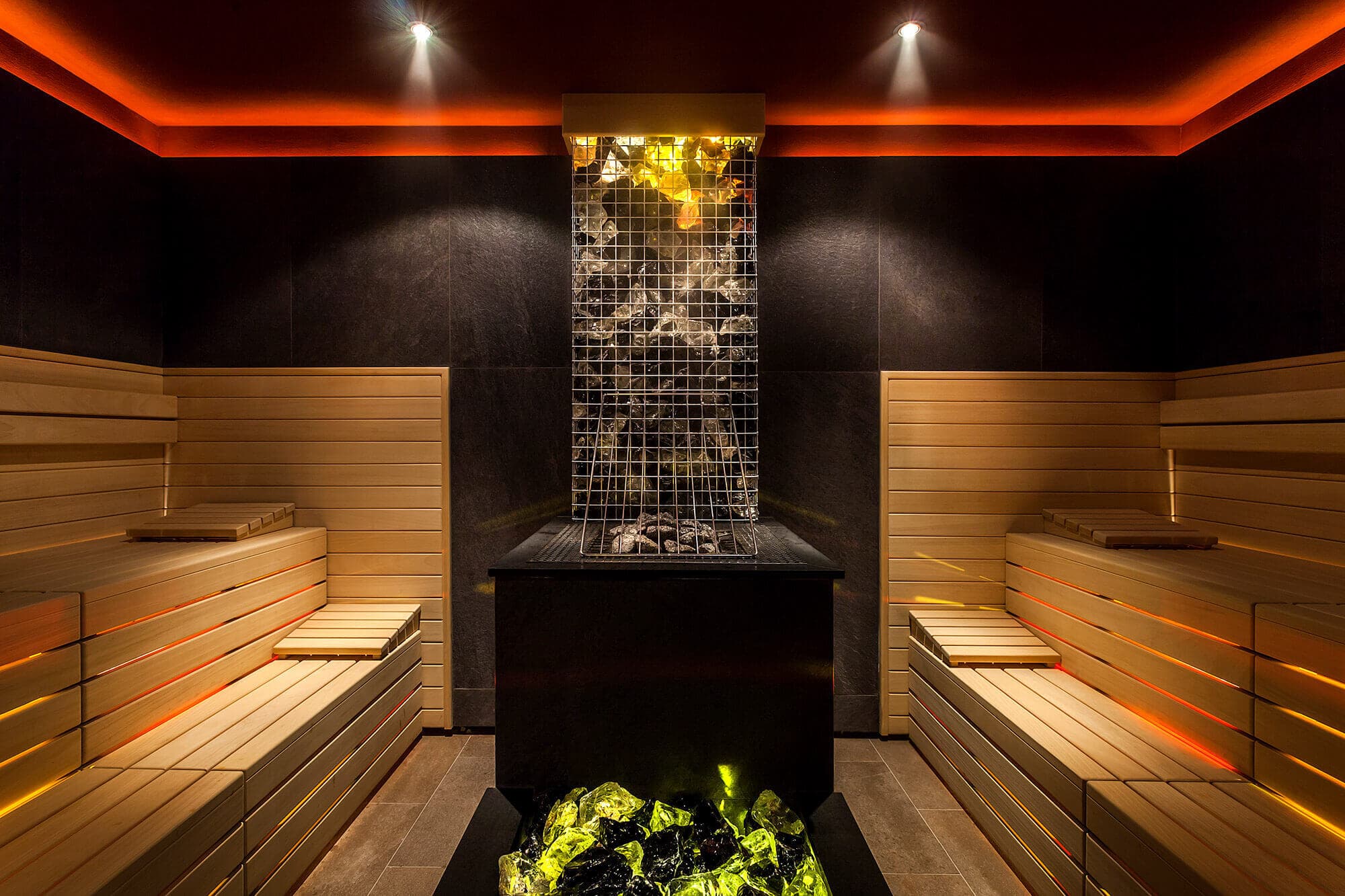 Striking lava stone sauna at Brimstone Hotel and Spa in Langdale, featuring illuminated volcanic rocks in cage design with dramatic orange ambient lighting, tiered wooden benches, and innovative Nordic-inspired thermal therapy in the heart of the Lake District Brimstone Spa