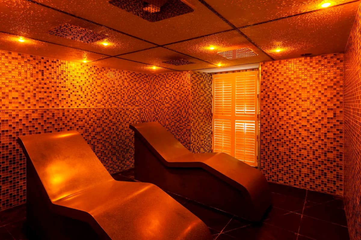 Luxurious tepidarium at Daffodil Hotel and Spa in Grasmere featuring golden amber mosaic tile walls creating warm therapeutic atmosphere, ergonomic heated ceramic loungers for gentle warming heat therapy, contemporary thermal facility in Lake District adults-only spa Daffodil Hotel Spa